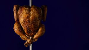 Goodbye, 2020 3 Whole rotisserie chicken cooked golden brown on a spit against a dark blue background.