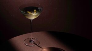appetiser. magazine 5 A chilled martini served in a coupe glass with a lemon twist, spotlighted on a dark, moody background.