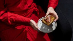 appetiser. magazine 9 A woman in a red dress holding a ceramic plate with a slice of Welsh rarebit topped with cured meat and chives.