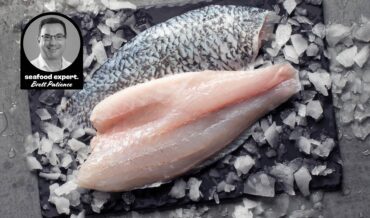 Close-up view of two barramundi fillets on a bed of ice. One fillet has its skin on, displaying a pattern of scales, while the other is skinless, revealing the pinkish-white flesh. A circular inset in the top left corner features a black and white photo of a person labeled "seafood expert. Brett Patience."